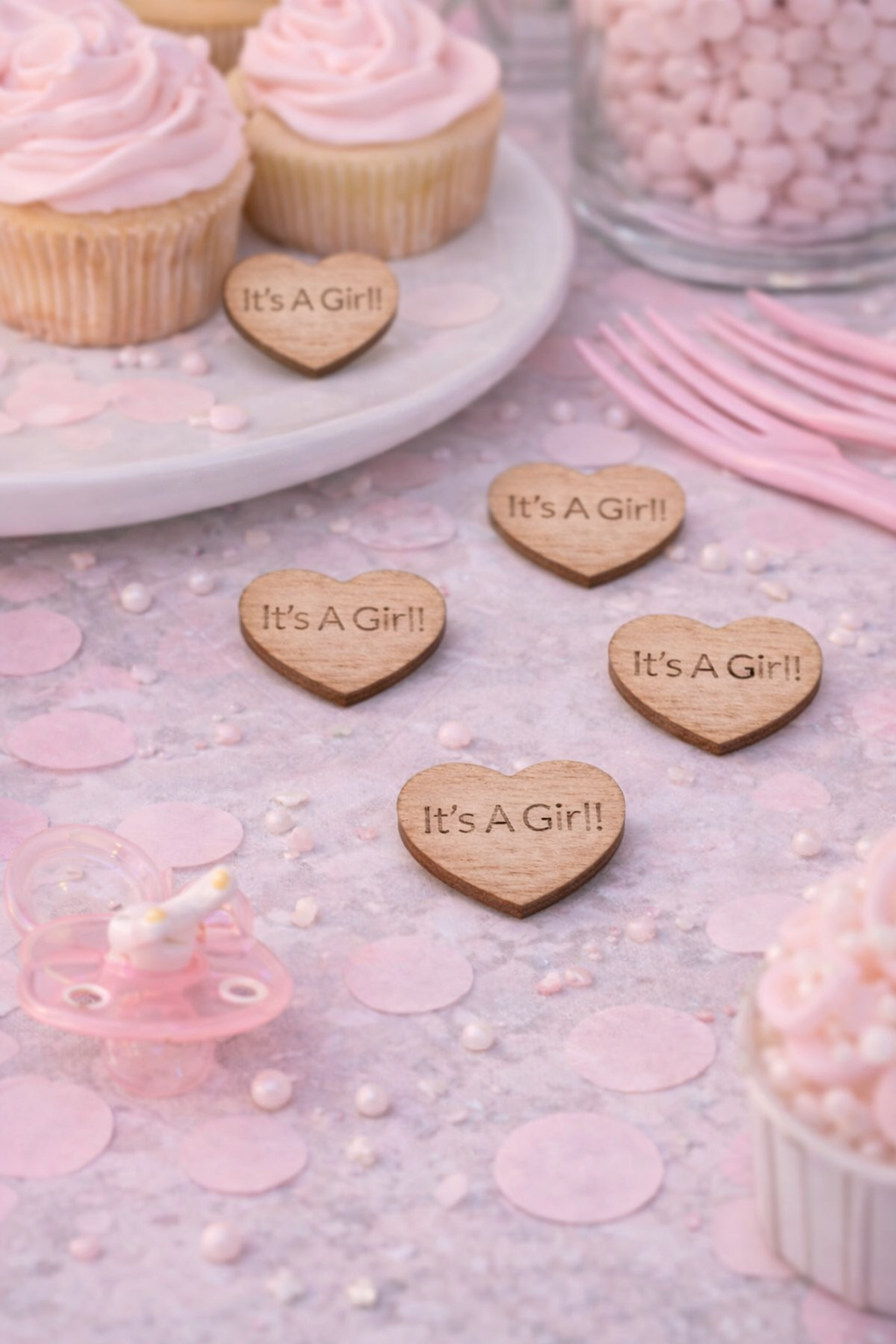 Wooden heart-shaped signs with 'It's a Girl!' text on a pink-themed background with cupcakes and candles.