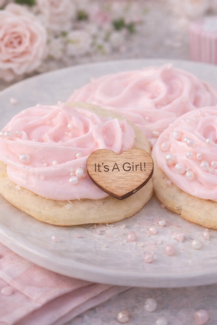 Decorative cookies with pink frosting and a heart-shaped sign on a marble surface with flowers in the background.